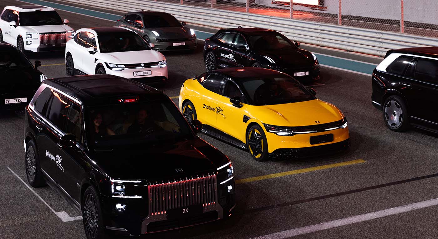 Black luxury Zeekr 009 SUV lined up next to a bright yellow electric sedan on an illuminated night race track.
